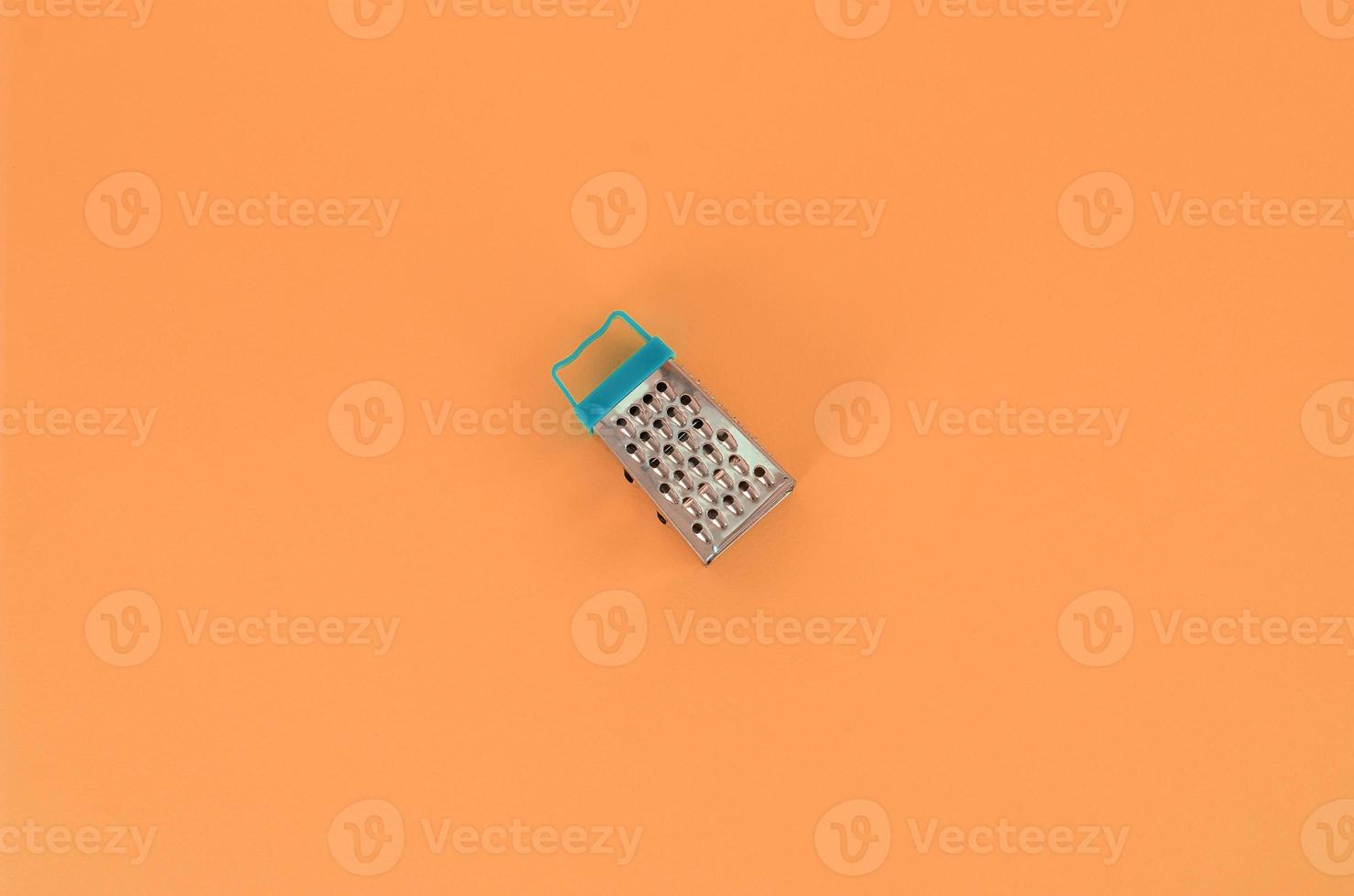 Stainless steel grater lies on a pastel colored paper. Kitchen accessories. Tools for cooking. Flat lay top view photo