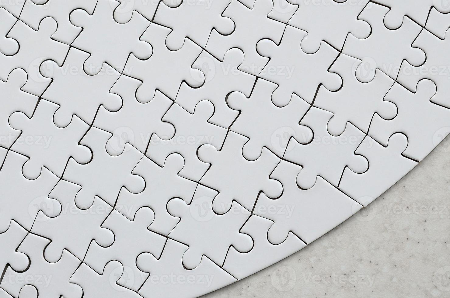 A white jigsaw puzzle in the complete form lies on a treated stone surface. Textured image with copy space photo