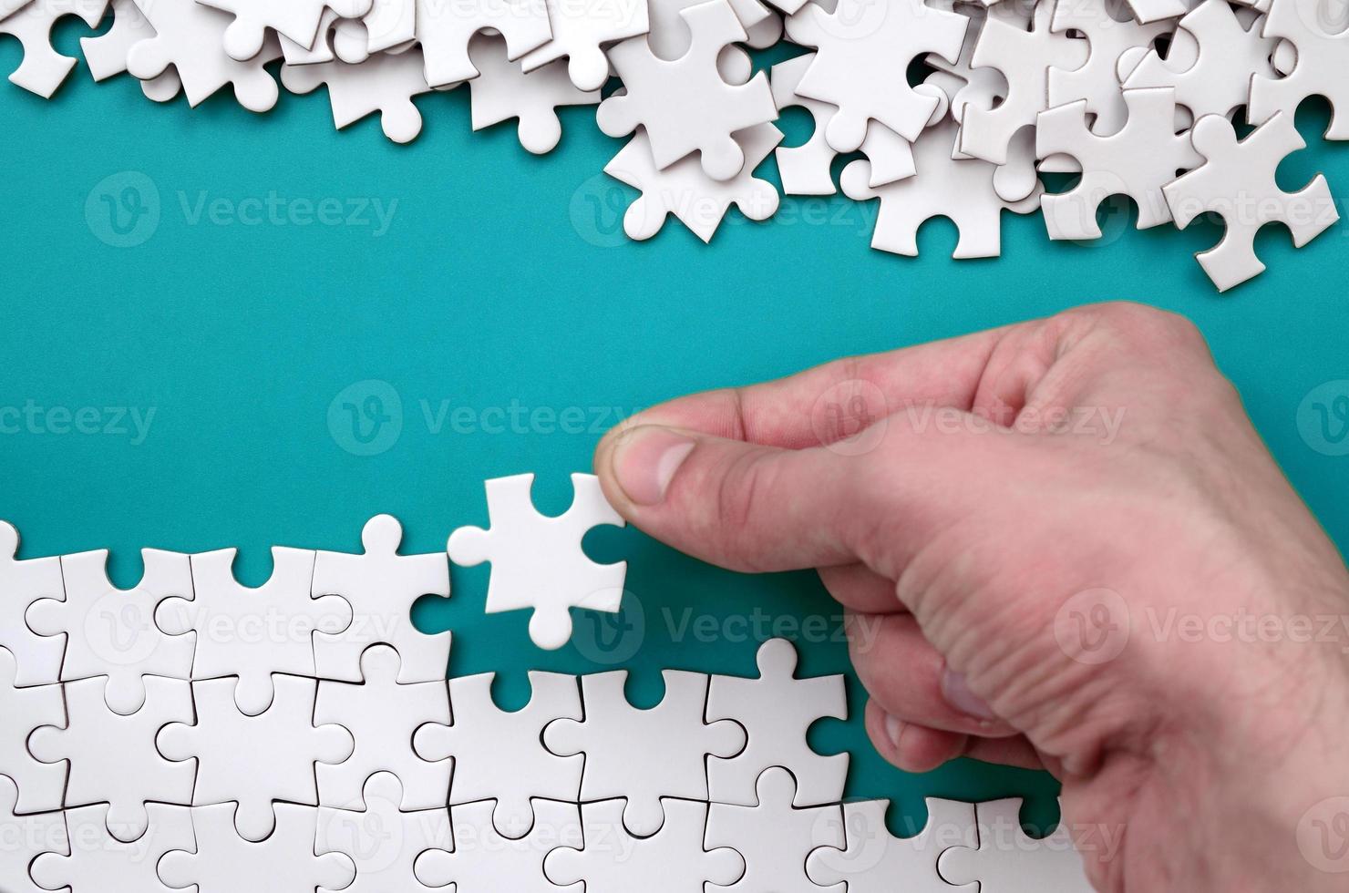 The hand folds a white jigsaw puzzle and a pile of uncombed puzzle pieces lies against the background of the blue surface. Texture photo with space for text