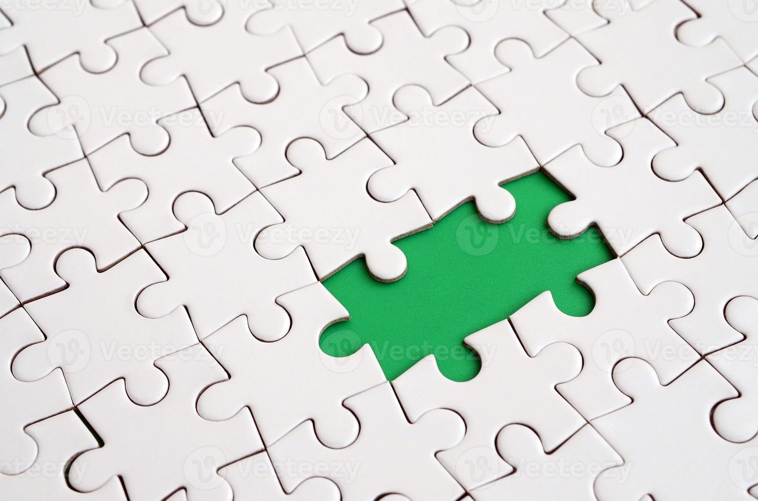 Close-up texture of a white jigsaw puzzle in assembled state with missing elements forming a green pad for text. Copy space photo