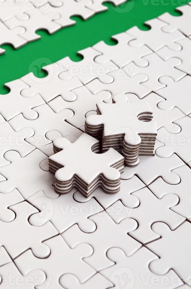 The green path is laid on the platform of a white folded jigsaw puzzle. The missing elements of the puzzle are stacked nearby. Texture image with space for text photo