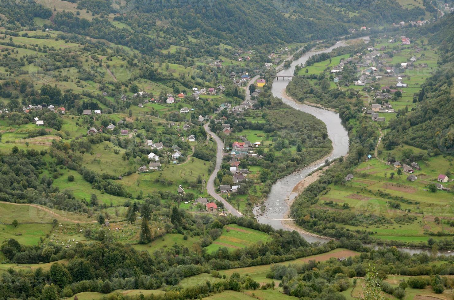 A beautiful view of the village of Mezhgorye, Carpathian region. A lot of residential buildings surrounded by high forest mountains and long river photo