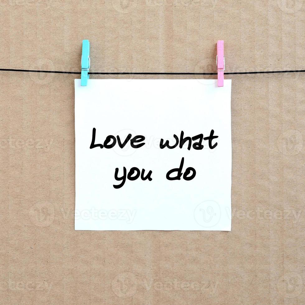 Love what you do. Note is written on a white sticker that hangs with a clothespin on a rope on a background of brown cardboard photo