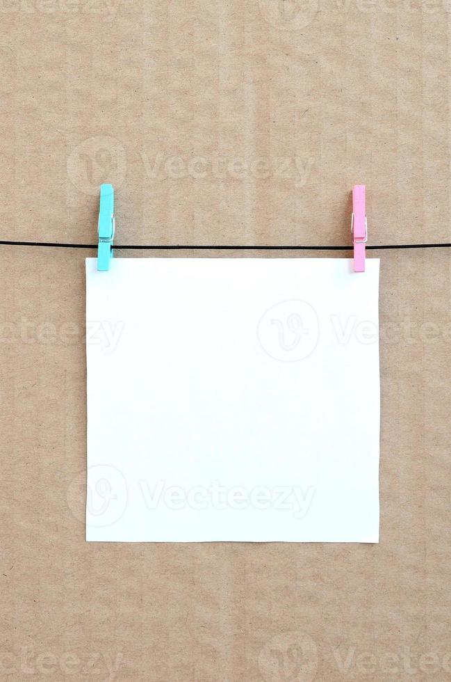 White blank card on rope on a brown cardboard background. Creative reminder, small sheet of paper on wooden clothespin, memo backdrop photo