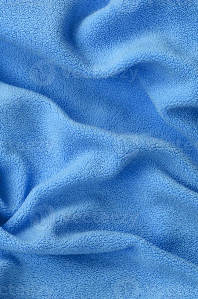 The blanket of furry blue fleece fabric. A background of light blue soft plush fleece material with a lot of relief folds photo