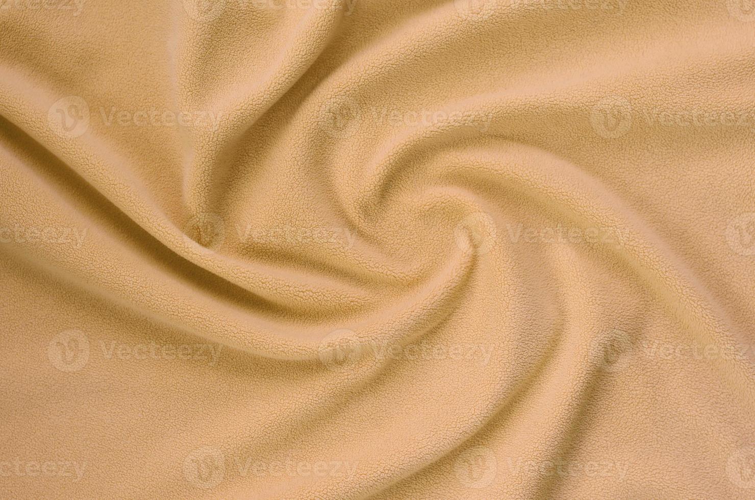 The blanket of furry orange fleece fabric. A background of light orange soft plush fleece material with a lot of relief folds photo