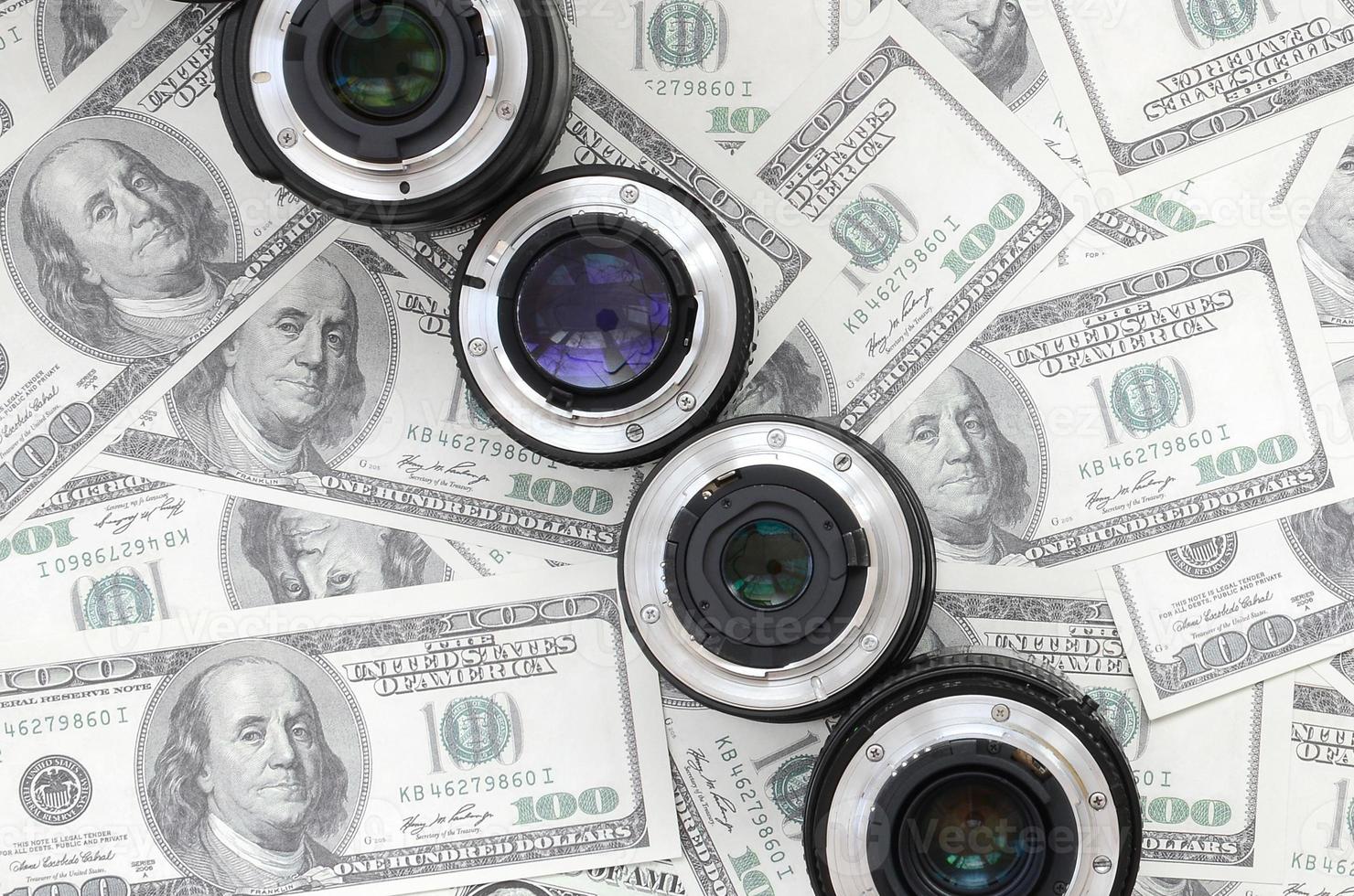 A few photographic lenses lies on the background of a lot of dollar bills. Space for text photo