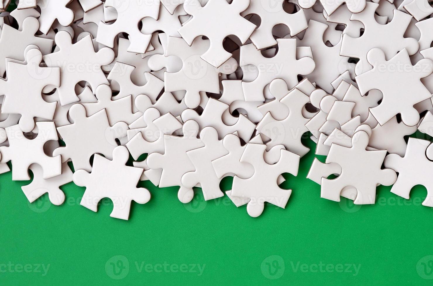 A pile of uncombed elements of a white jigsaw puzzle lies on the background of a green surface. Texture photo with copy space for text