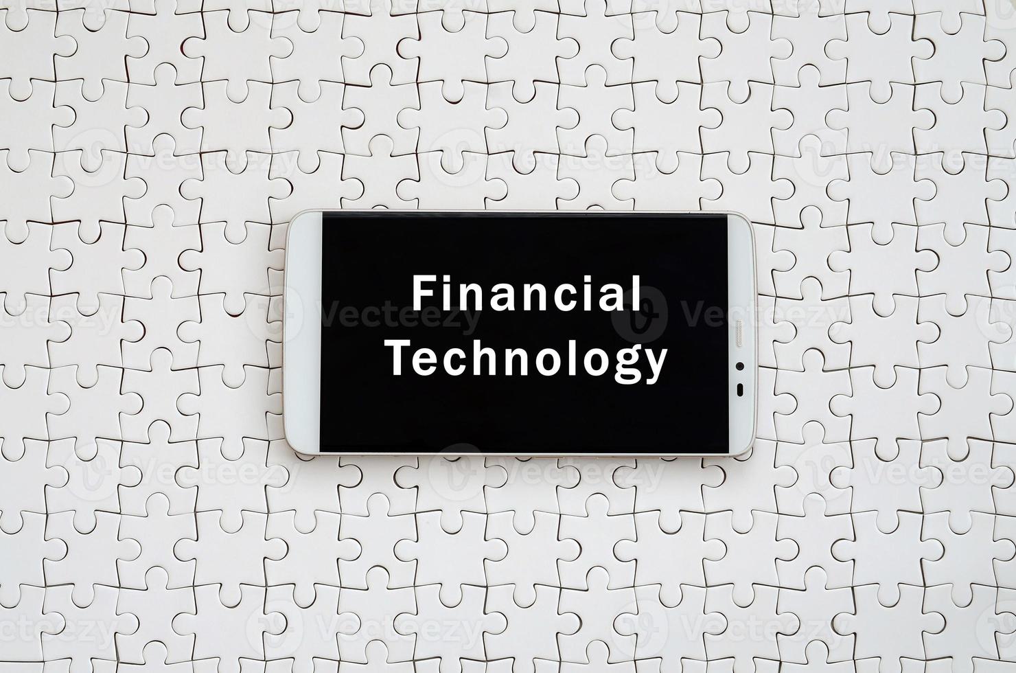 A modern big smartphone with a touch screen lies on a white jigsaw puzzle in an assembled state with inscription. Financial technology photo
