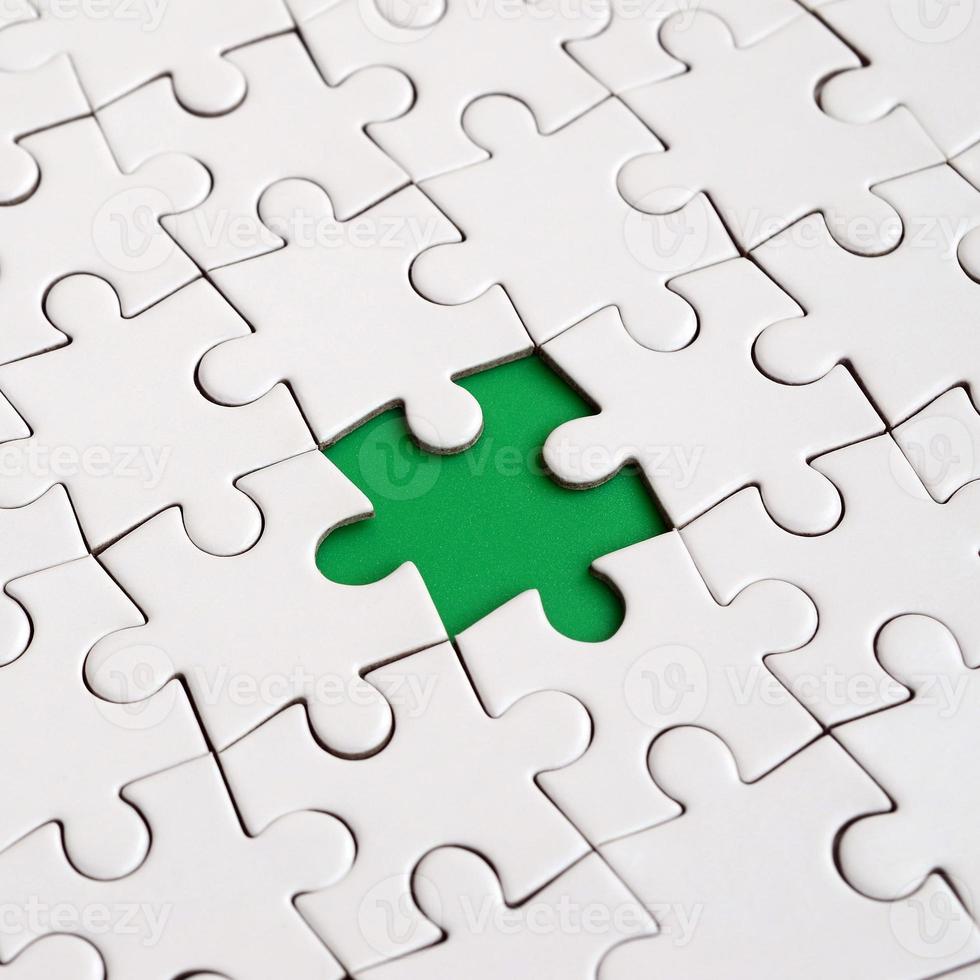 Close-up texture of a white jigsaw puzzle in assembled state with missing elements forming a green pad for text. Copy space photo