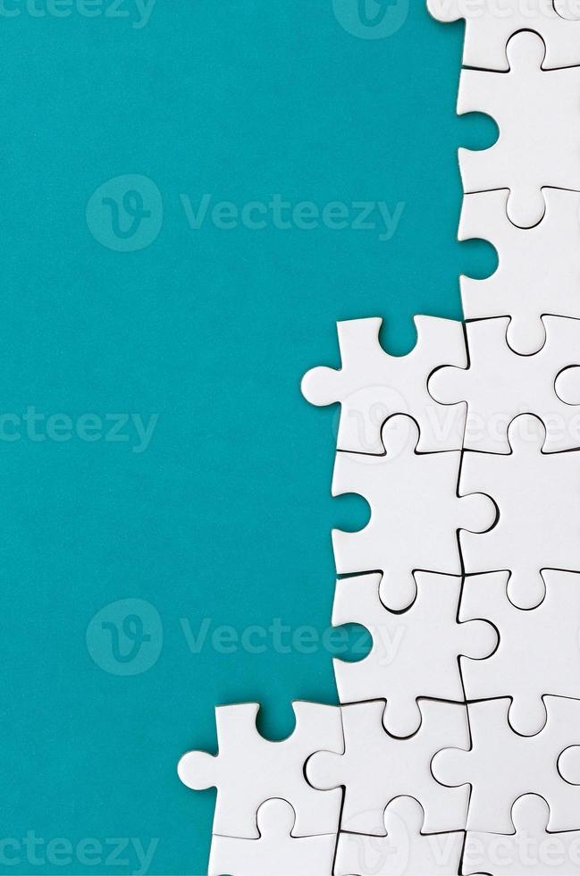 Fragment of a folded white jigsaw puzzle on the background of a blue plastic surface. Texture photo with copy space for text