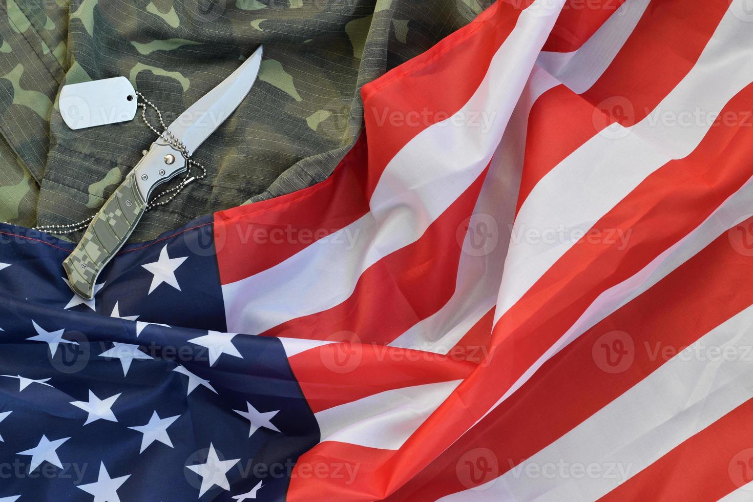 la ficha de la etiqueta de perro del ejército y el cuchillo se encuentran en el viejo uniforme de camuflaje y la bandera de los Estados Unidos doblada foto