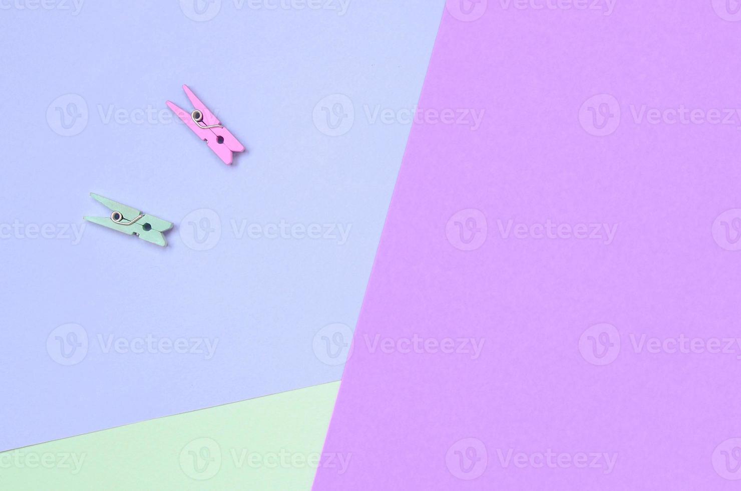 Two colored wooden pegs lie on texture background of fashion pastel violet, turquoise and pink colors paper photo