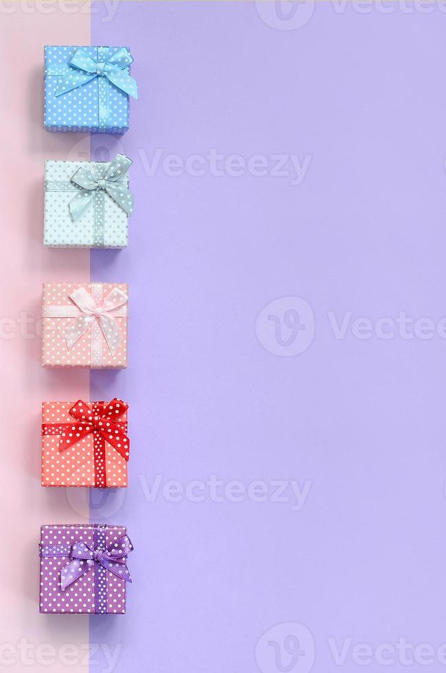 Small gift boxes of different colors with ribbons lies on a violet and pink color background photo