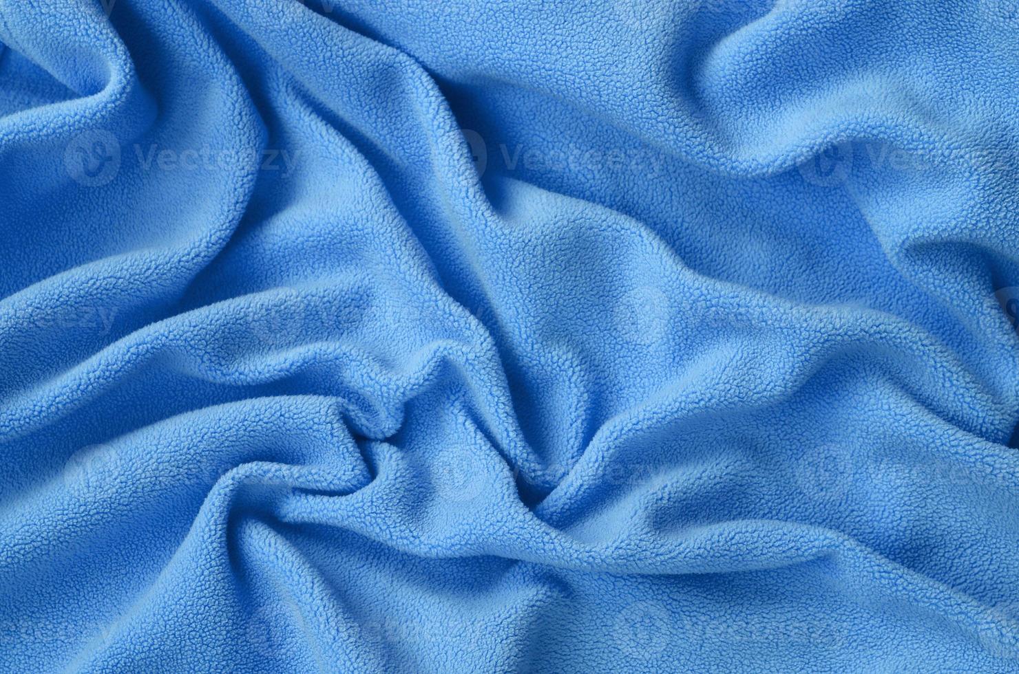The blanket of furry blue fleece fabric. A background of light blue soft plush fleece material with a lot of relief folds photo