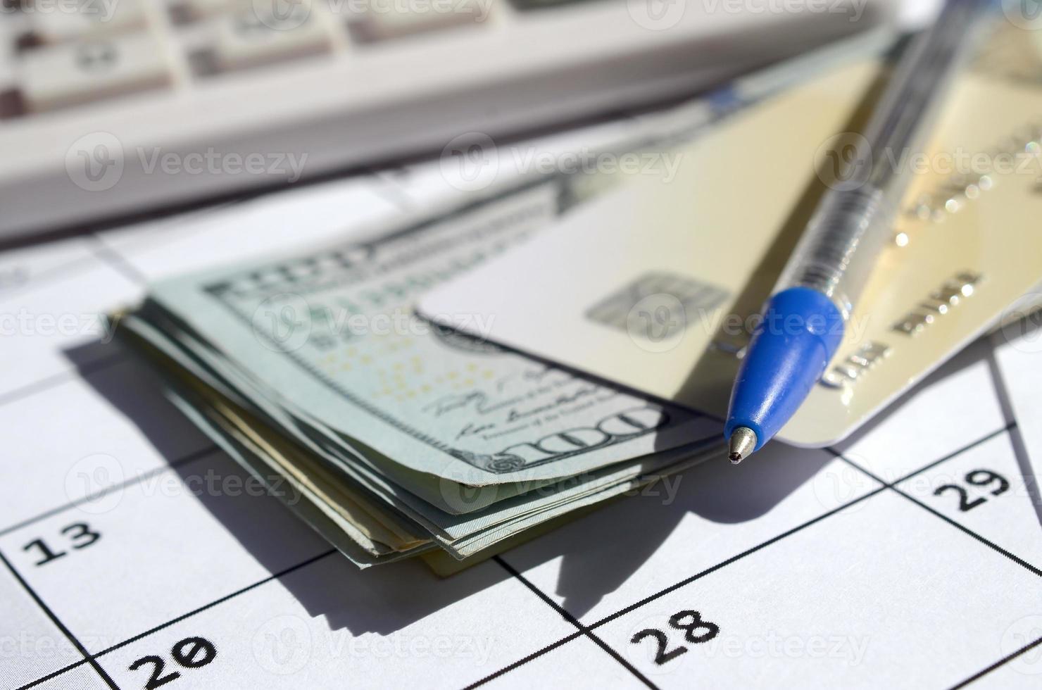 Pen and credit card on many hundred US dollar bills and calculator on calendar page close up photo