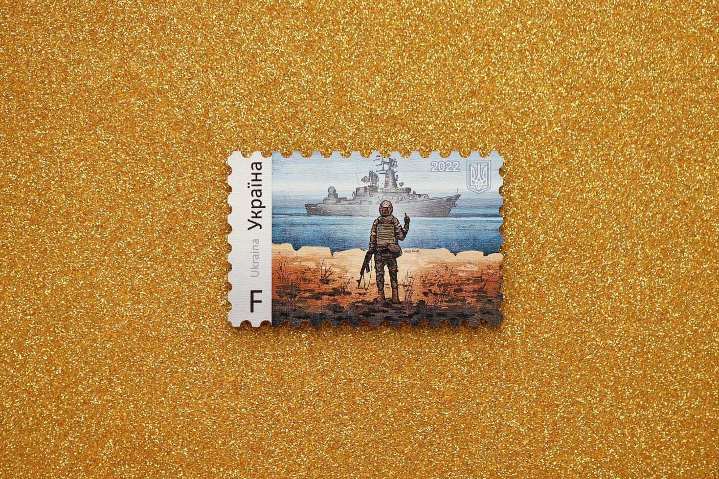 TERNOPIL, UKRAINE - SEPTEMBER 2, 2022 Famous Ukrainian postmark with russian warship and ukrainian soldier as wooden souvenir on golden glitter background photo