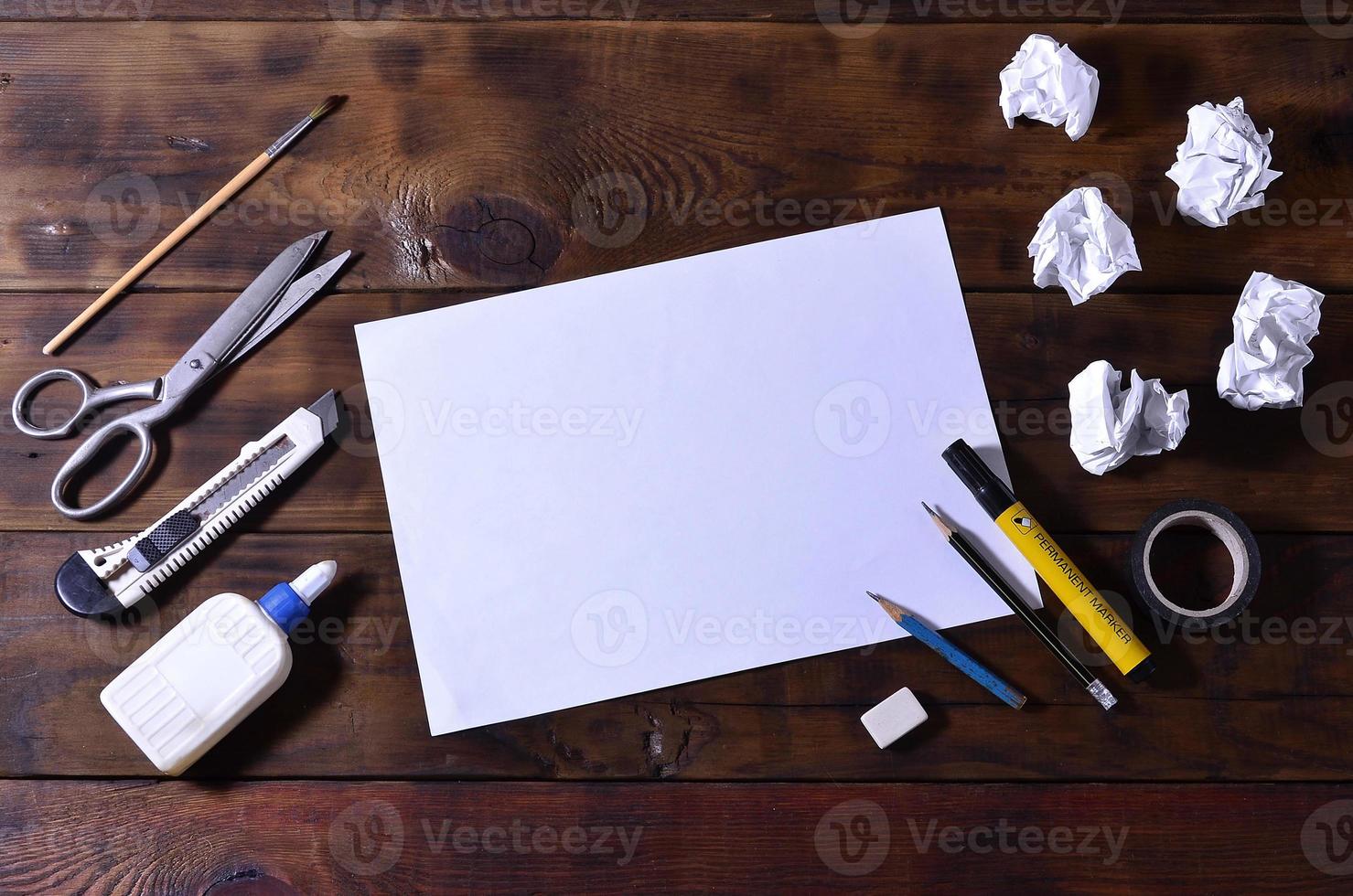 un bodegón de escuela u oficina con una hoja de papel en blanco y muchos suministros de oficina. los útiles escolares se encuentran sobre un fondo de madera marrón. lugar para texto foto