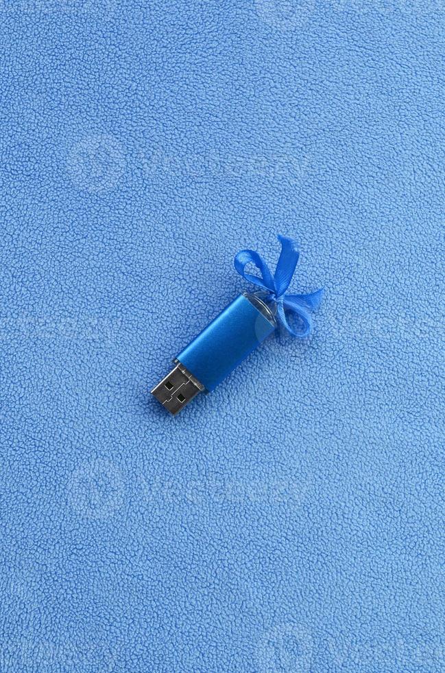 Brilliant blue usb flash memory card with a blue bow lies on a blanket of soft and furry light blue fleece fabric. Classic female gift design for a memory card photo