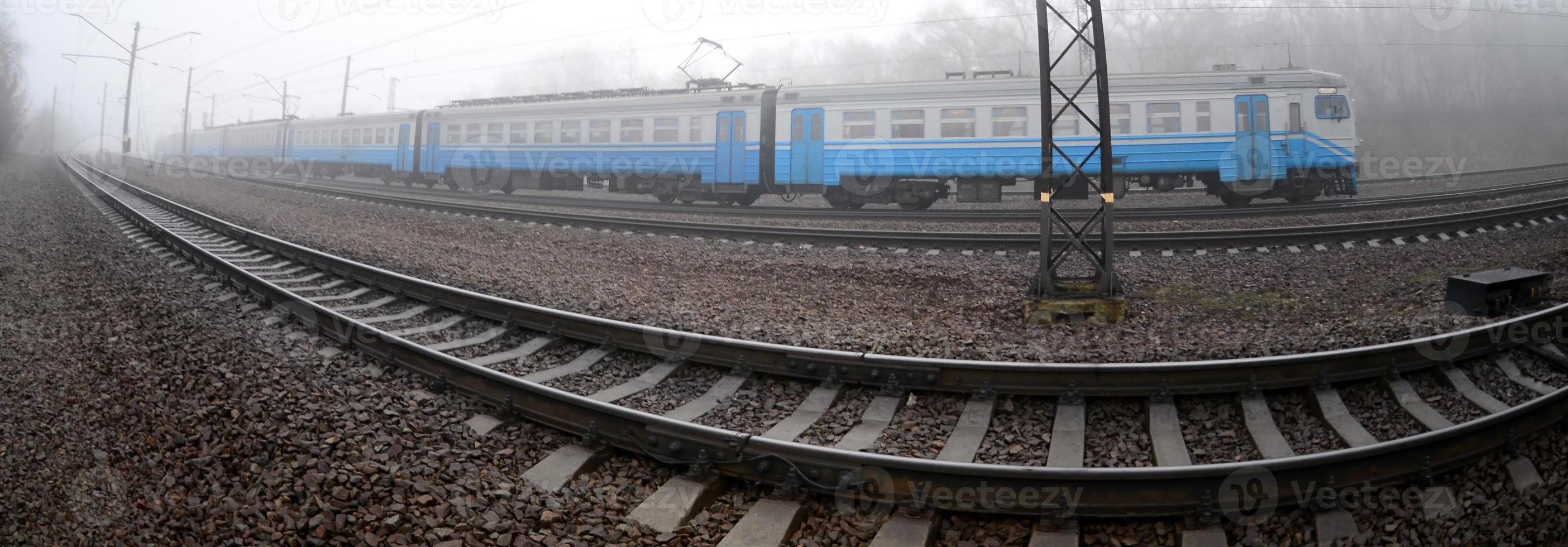 The Ukrainian suburban train rushes along the railway in a misty morning. Fisheye photo with increased distortion