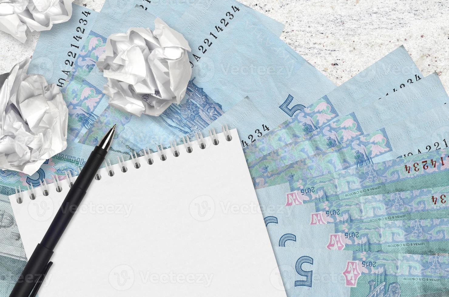 5 Ukrainian hryvnias bills and balls of crumpled paper with blank notepad. Bad ideas or less of inspiration concept. Searching ideas for investment photo