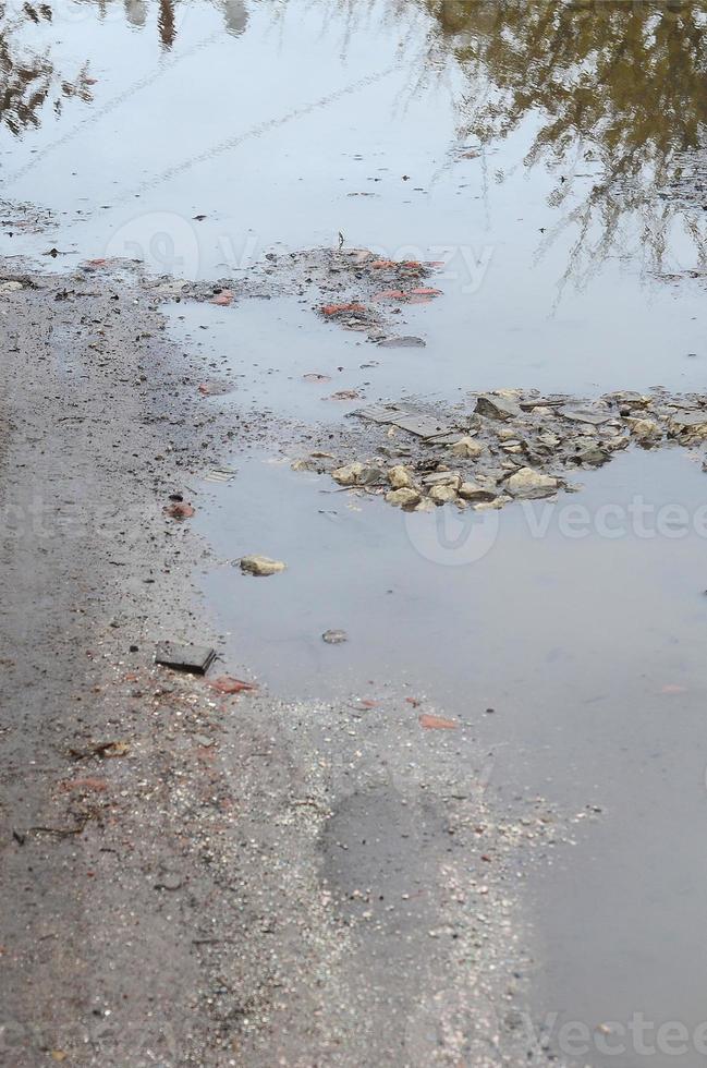 Photo of a fragment of a destroyed road with large puddles in rainy weather