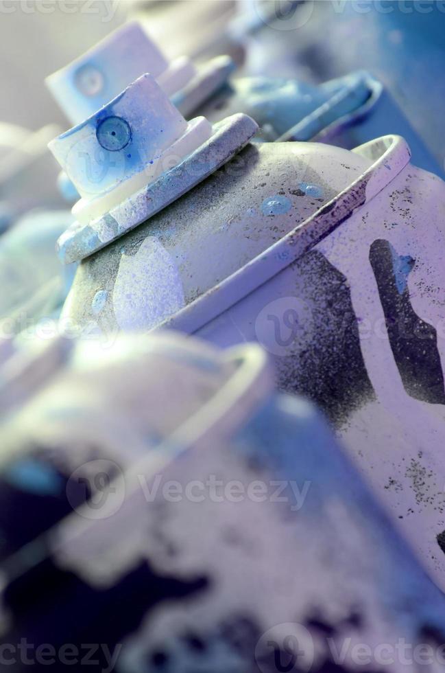 A lot of dirty and used aerosol cans of bright blue paint. Macro photograph with shallow depth of field. Selective focus on the spray nozzle photo