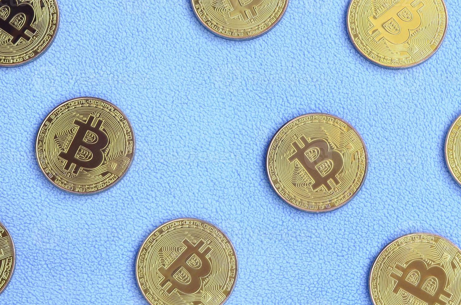 Many golden bitcoins lies on a blanket made of soft and fluffy light blue fleece fabric. Physical visualization of virtual crypto currency photo
