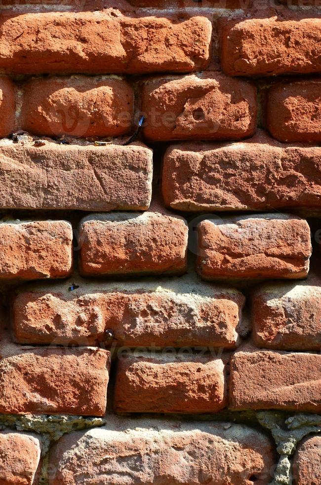 Vertical wall texture of several rows of very old brickwork made of red