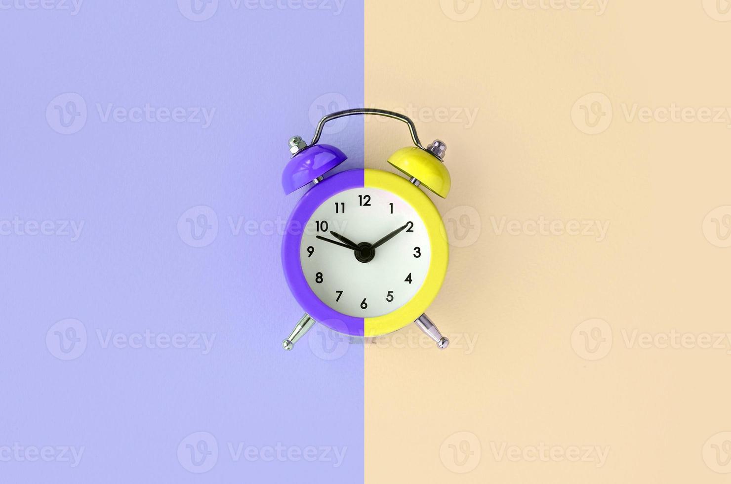 A small alarm clock is located between the violet and cream background areas photo
