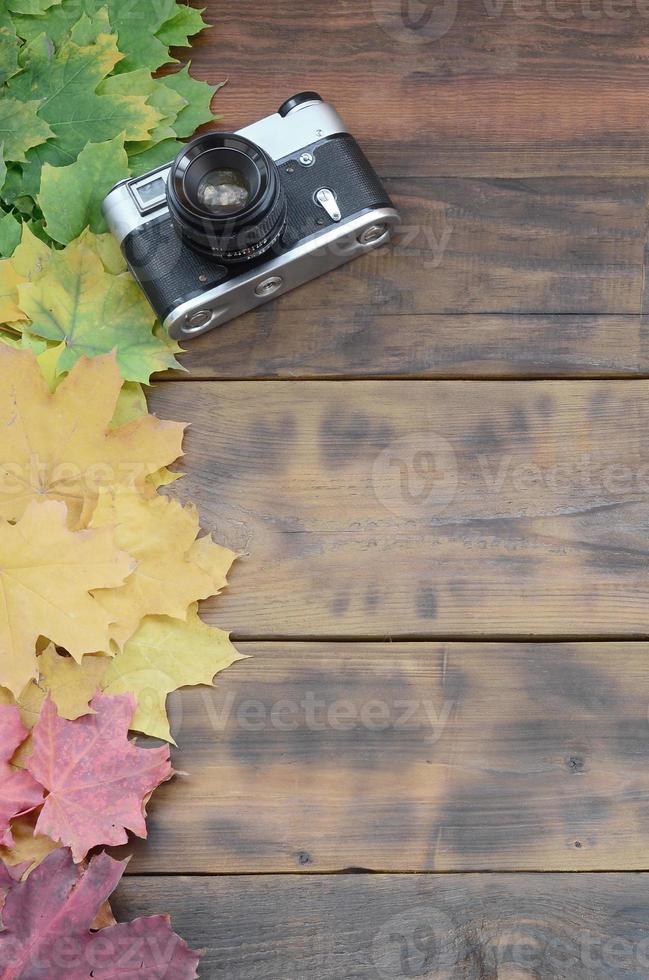 The old camera among a set of yellowing fallen autumn leaves on a background surface of natural wooden boards of dark brown color photo