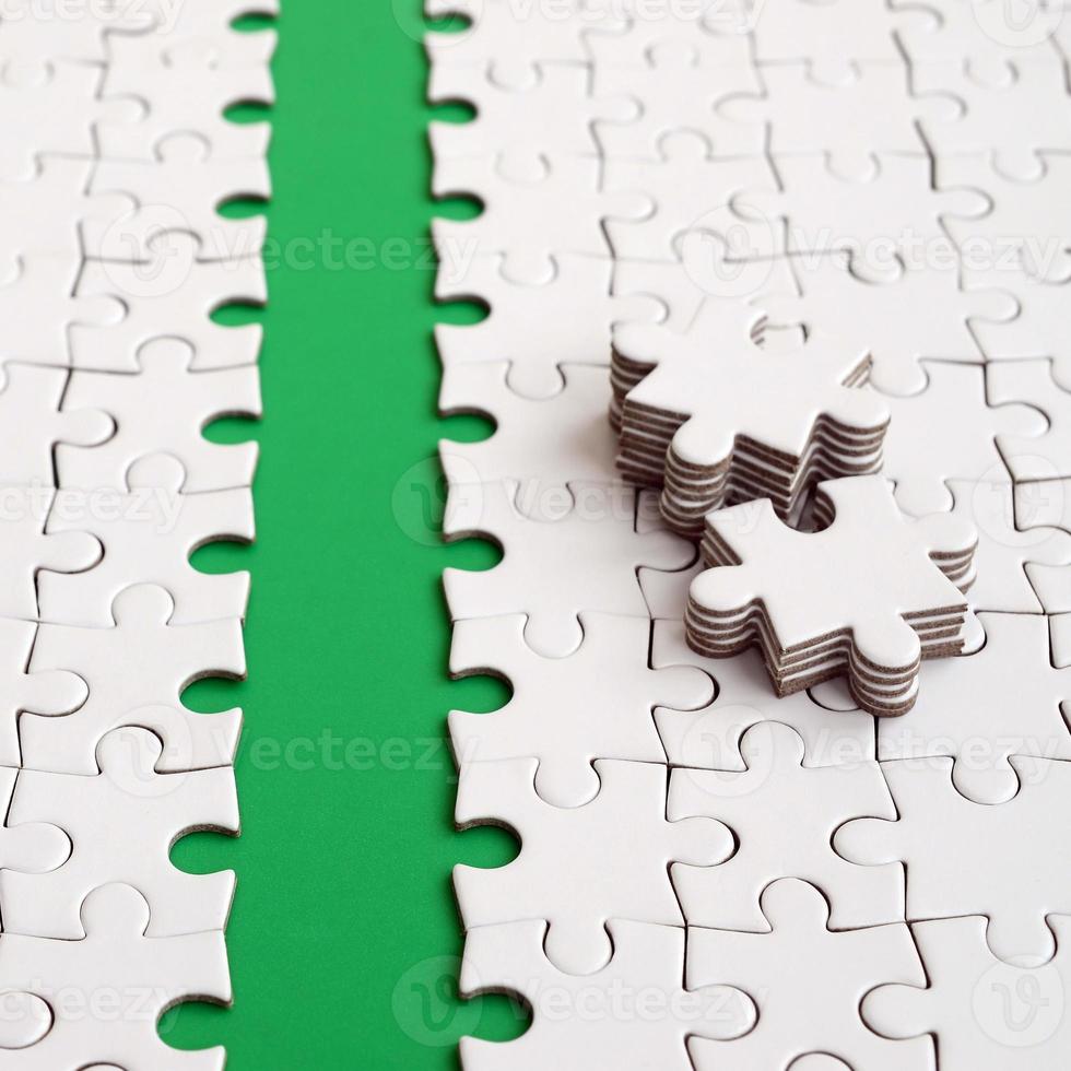 The green path is laid on the platform of a white folded jigsaw puzzle. The missing elements of the puzzle are stacked nearby. Texture image with space for text photo