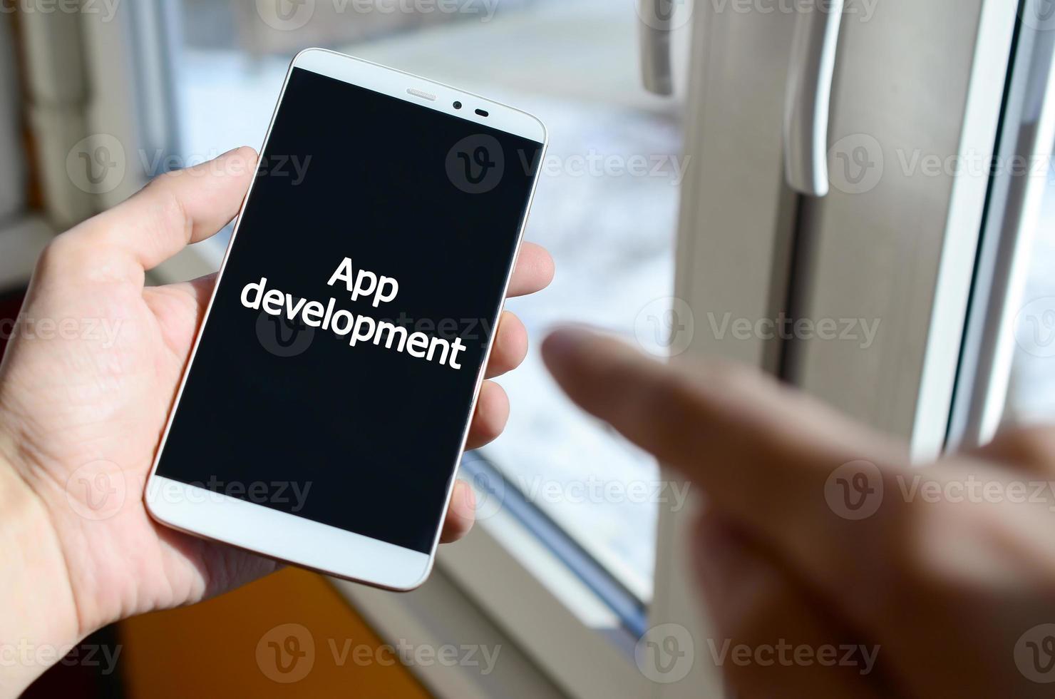 A person sees a white inscription on a black smartphone display that holds in his hand. App development photo