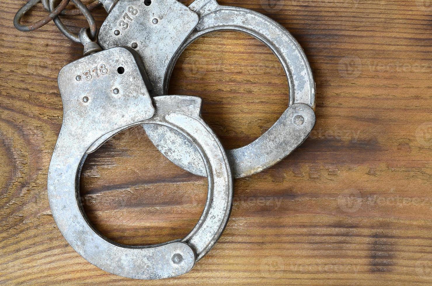 Old and rusty police handcuffs lie on a scratched wooden surface. The concept of an old crime photo