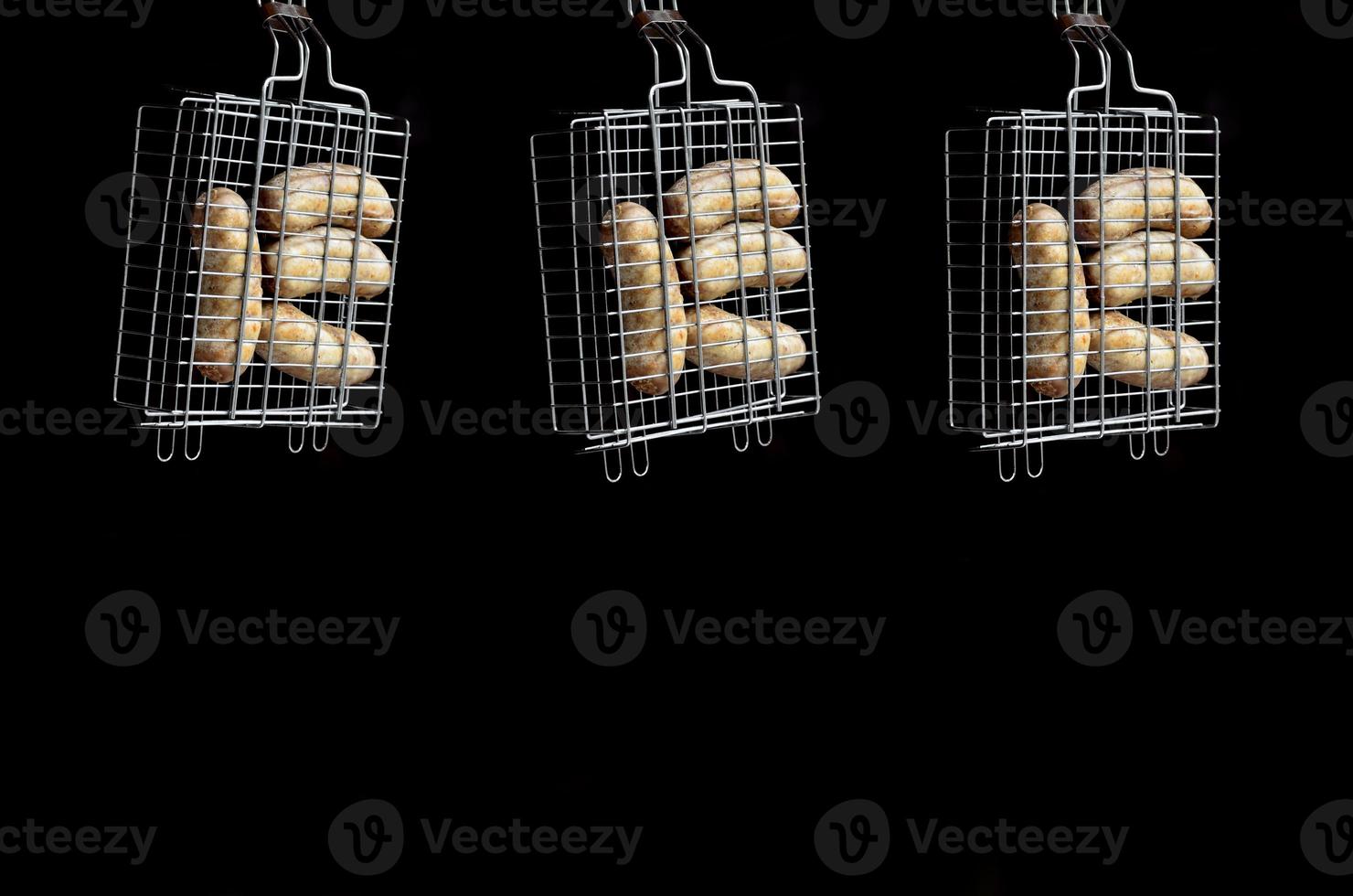 A small hand grill is filled with fried thick sausages on a dark background photo