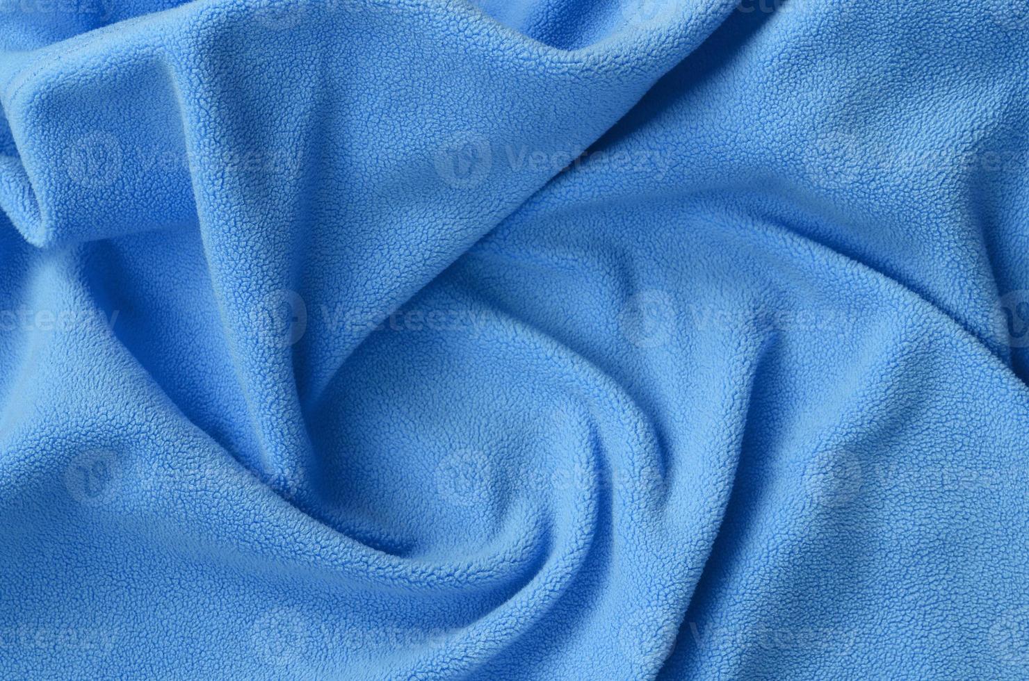 The blanket of furry blue fleece fabric. A background of light blue soft plush fleece material with a lot of relief folds photo