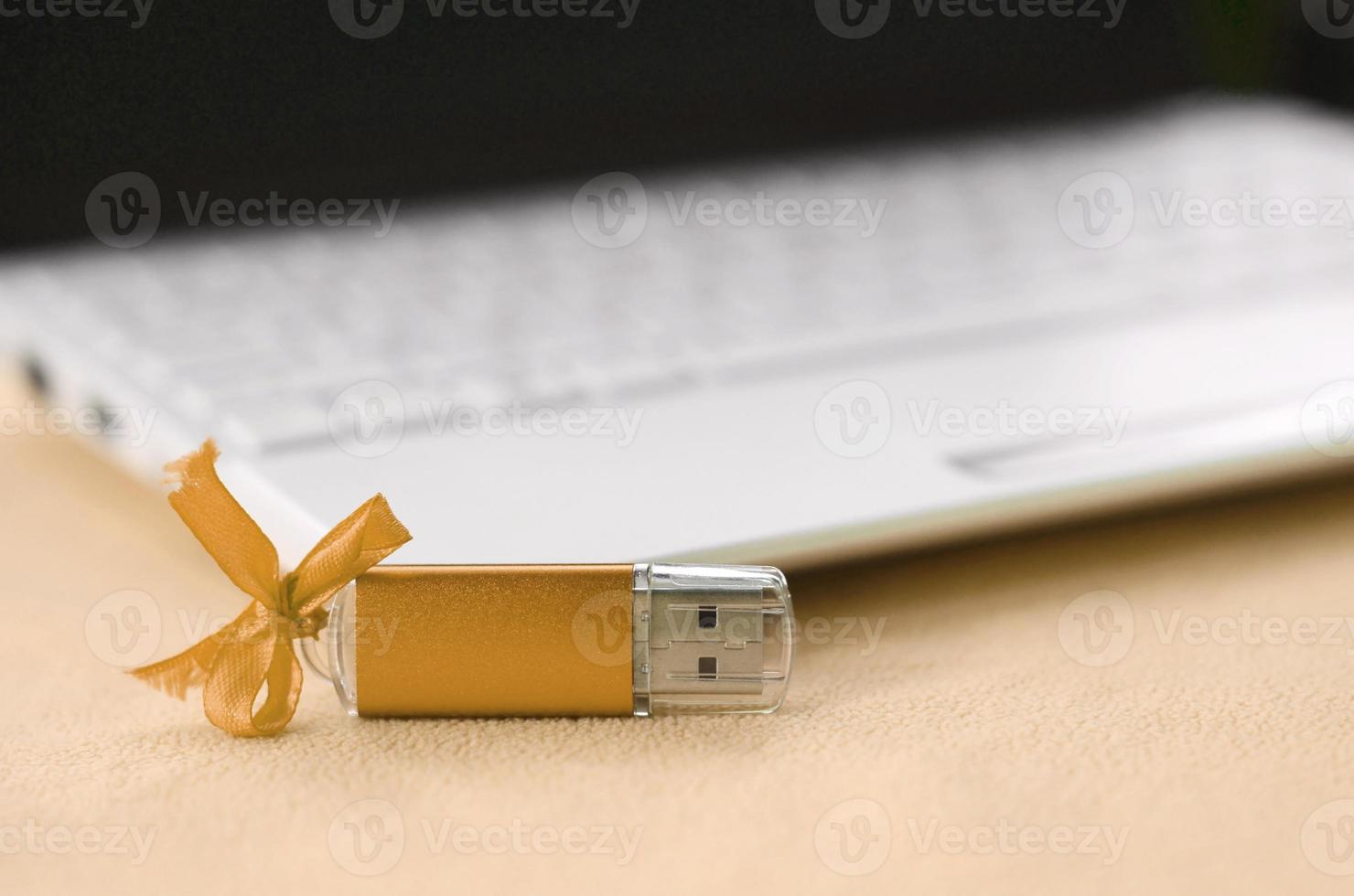 la tarjeta de memoria flash usb naranja con un lazo se encuentra sobre una manta de tela suave y peluda de color naranja claro al lado de una computadora portátil blanca. diseño clásico de regalo femenino para una tarjeta de memoria foto