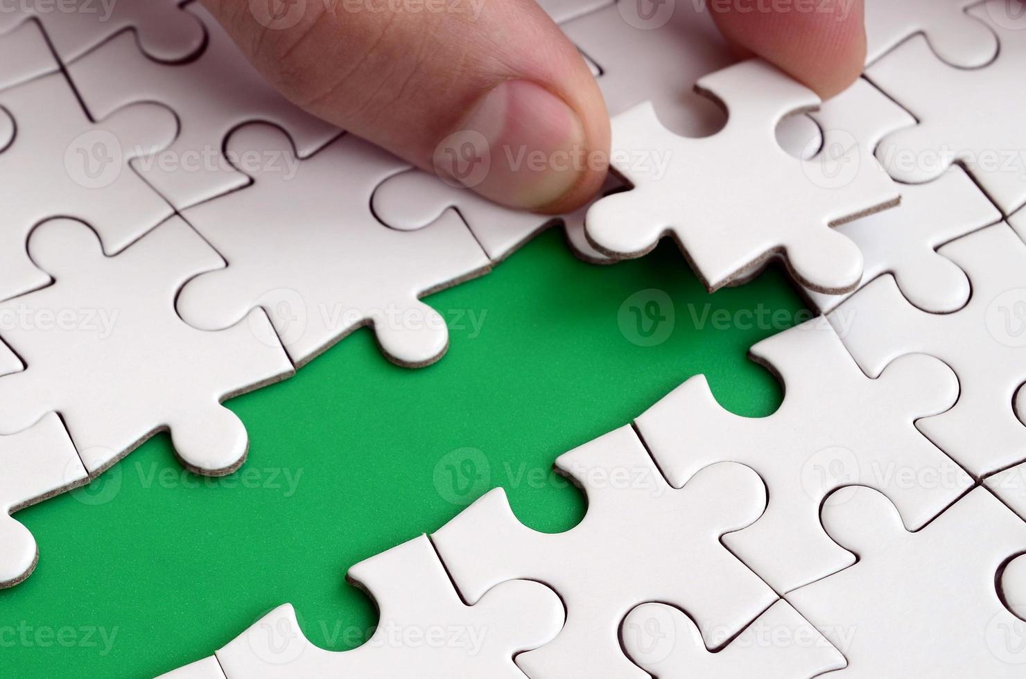 The human hand paves the way to the surface of the jigsaw puzzle, forming a green space. The concept of overcoming the difficulties on the way to success photo