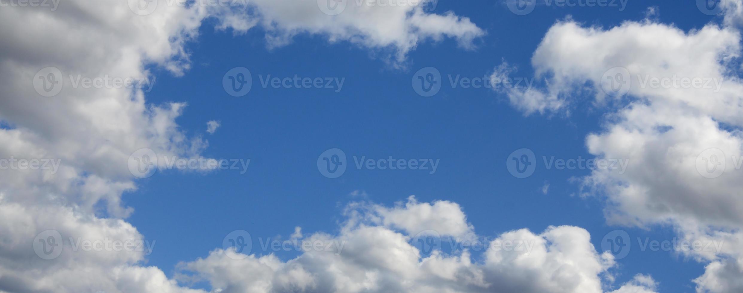 The blue sky with a lot of white clouds of different sizes, forming a frame around the cloudless area photo