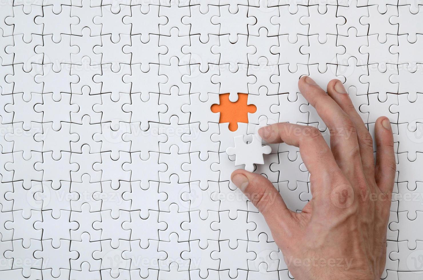 The texture of a white jigsaw puzzle in the assembled state with one missing element that the male hand puts in photo