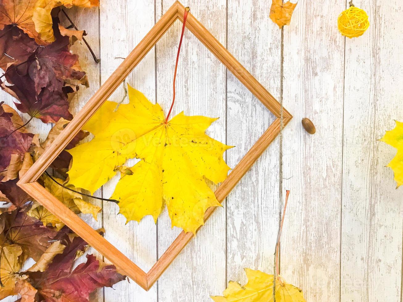 Wooden rectangular picture frame and yellow colorful natural autumn leaves, maple on the background of wooden boards. The background. Texture photo