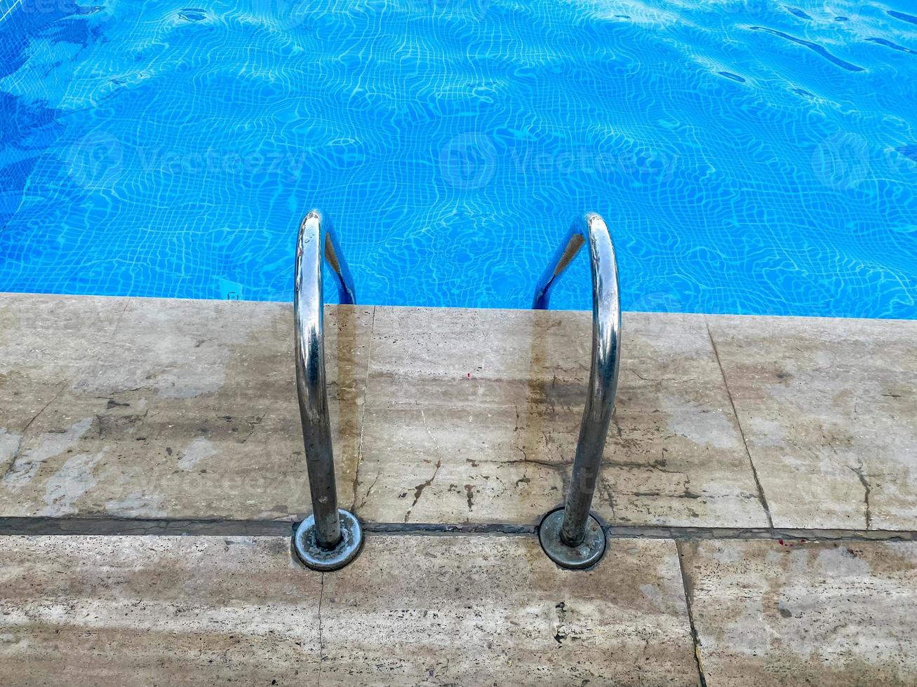 Chrome-plated metal staircase with railing to descend into the pool for swimming and bathing with warm clean blue clear water in a hotel in a tropical paradise resort photo
