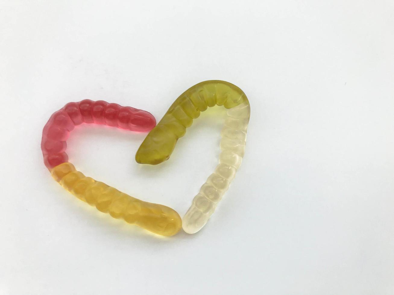 gusanos de mermelada. gusanos gelatinosos, multicolores entrelazados en forma de corazón. gusano amarillo-rojo y verde-blanco sobre un fondo blanco mate. delicioso y apetitoso postre foto