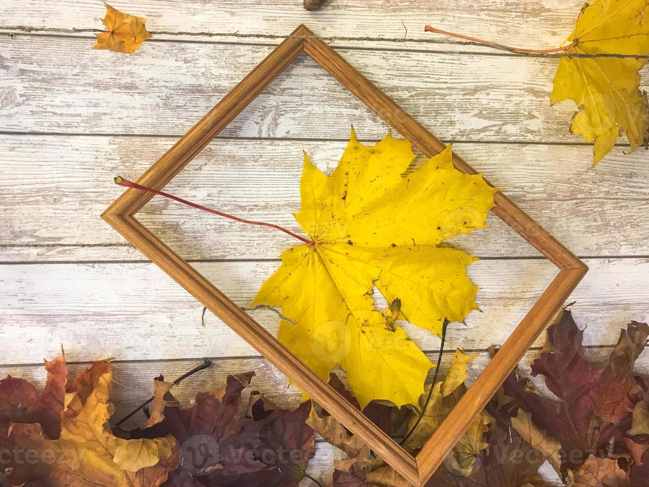 Wooden rectangular picture frame and yellow colorful natural autumn leaves, maple on the background of wooden boards. The background. Texture photo