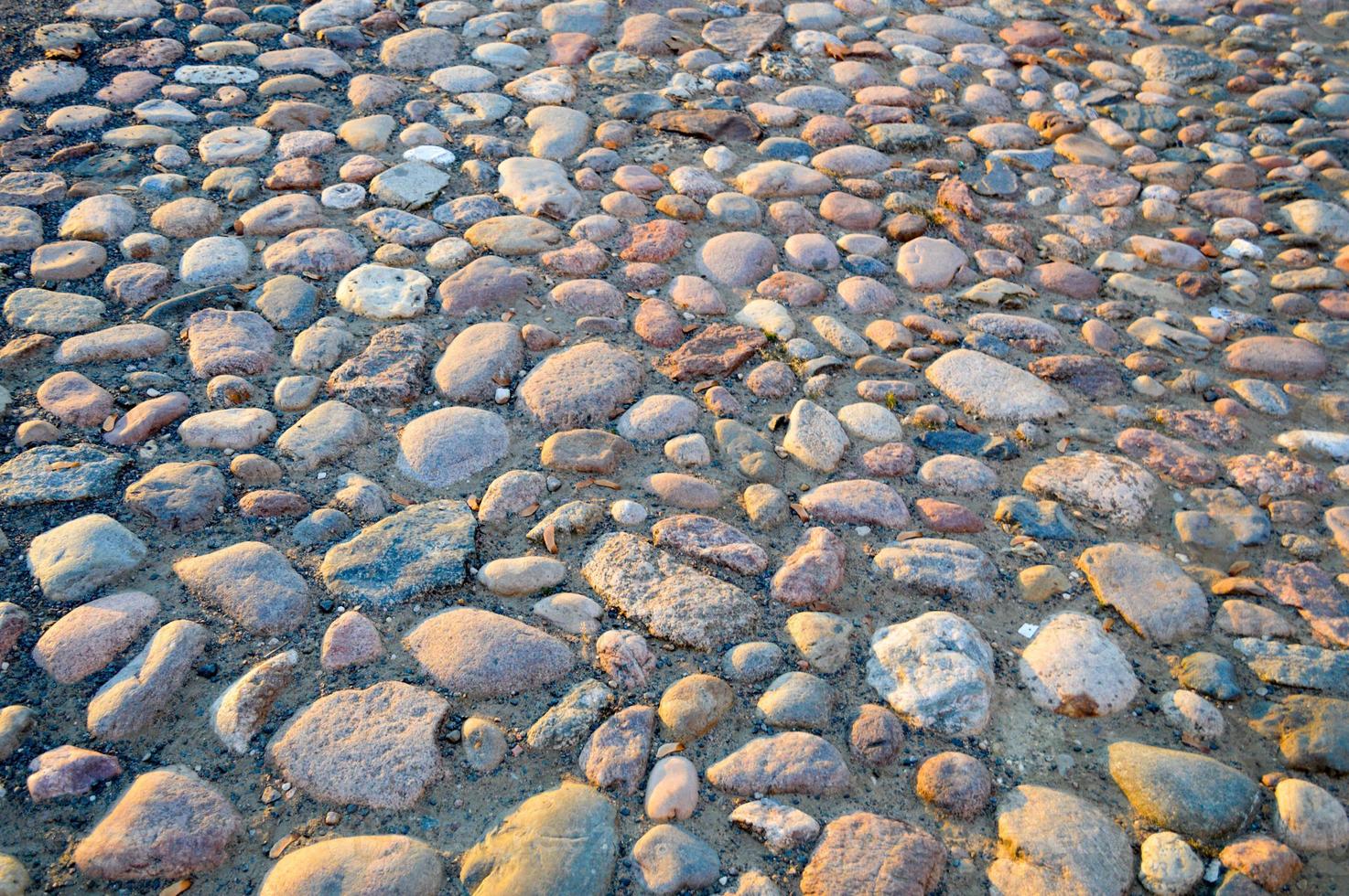 The texture of the stone road, pavement, walls of large gray old medieval round strong stones, cobblestones. The background photo