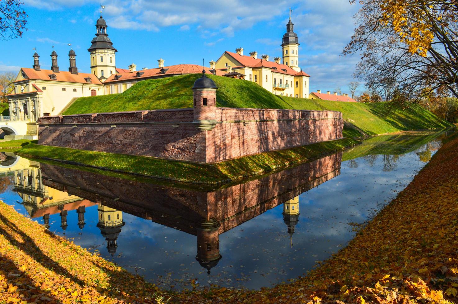 Old, ancient medieval castle with spiers and towers, walls of stone and brick surrounded by a protective moat with water in the center of Europe. Baroque style architecture photo