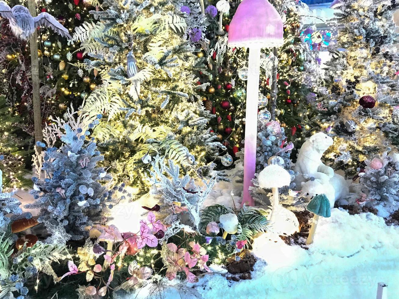 new year cute decorations for the shopping center. artificial Christmas trees with lighting. spruce covered with artificial snow. next to a pink mushroom with a round cap photo