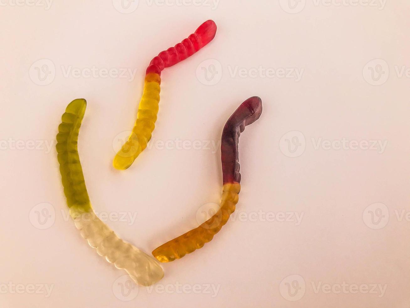 gummy worms of different colors lie on a pink matte background. gelatinous sweetness. leaf-shaped worms, circling with steam. decoration of cakes and pastries, dessert for tea and coffee photo