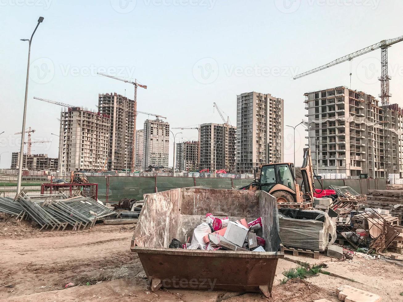 industrial site. construction of a large residential complex. in the center is a large, rusty metal container for collecting bulky waste. next to construction equipment photo