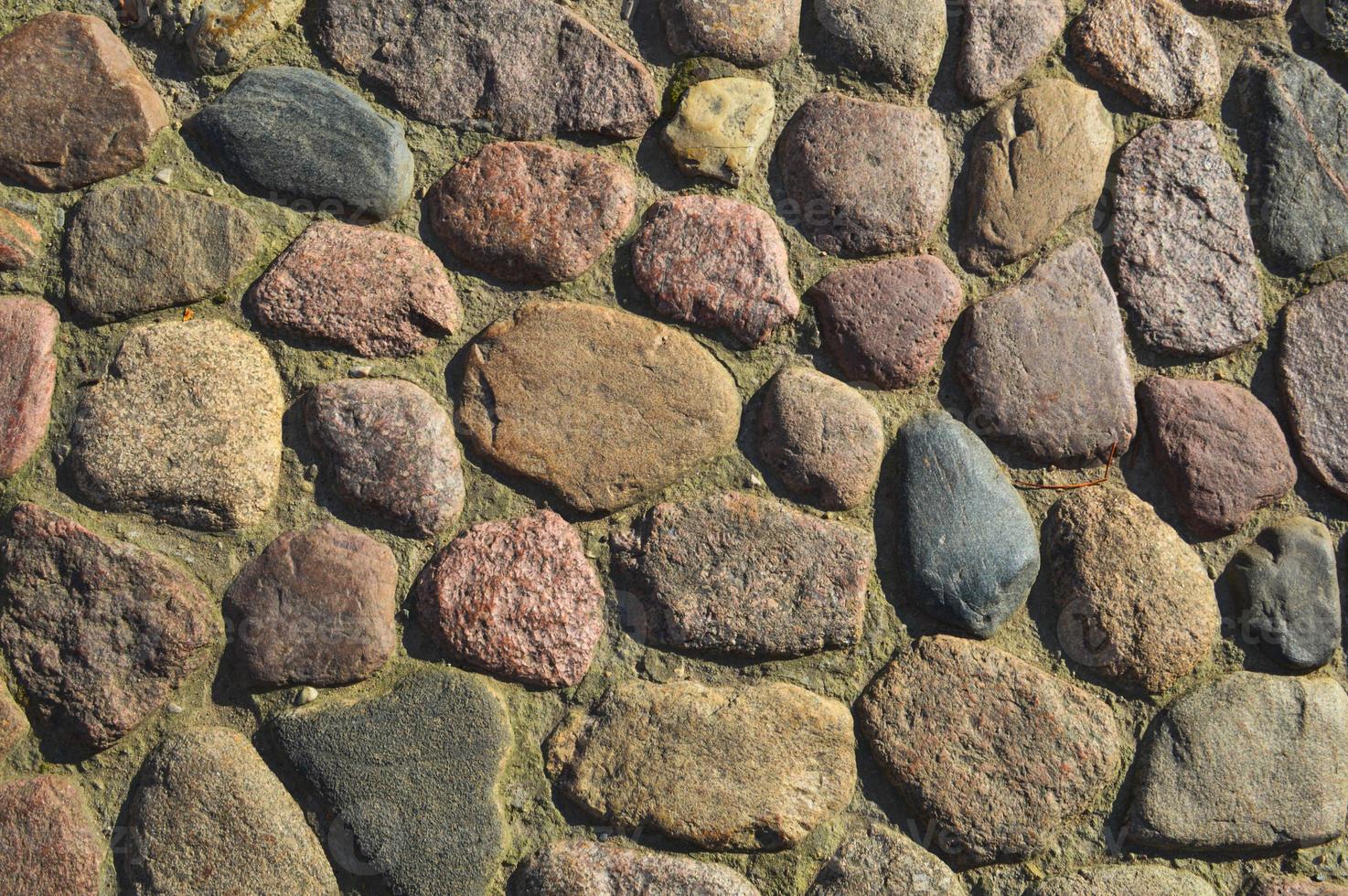 The texture of the stone road, pavement, walls of large gray old medieval round strong stones, cobblestones. The background photo